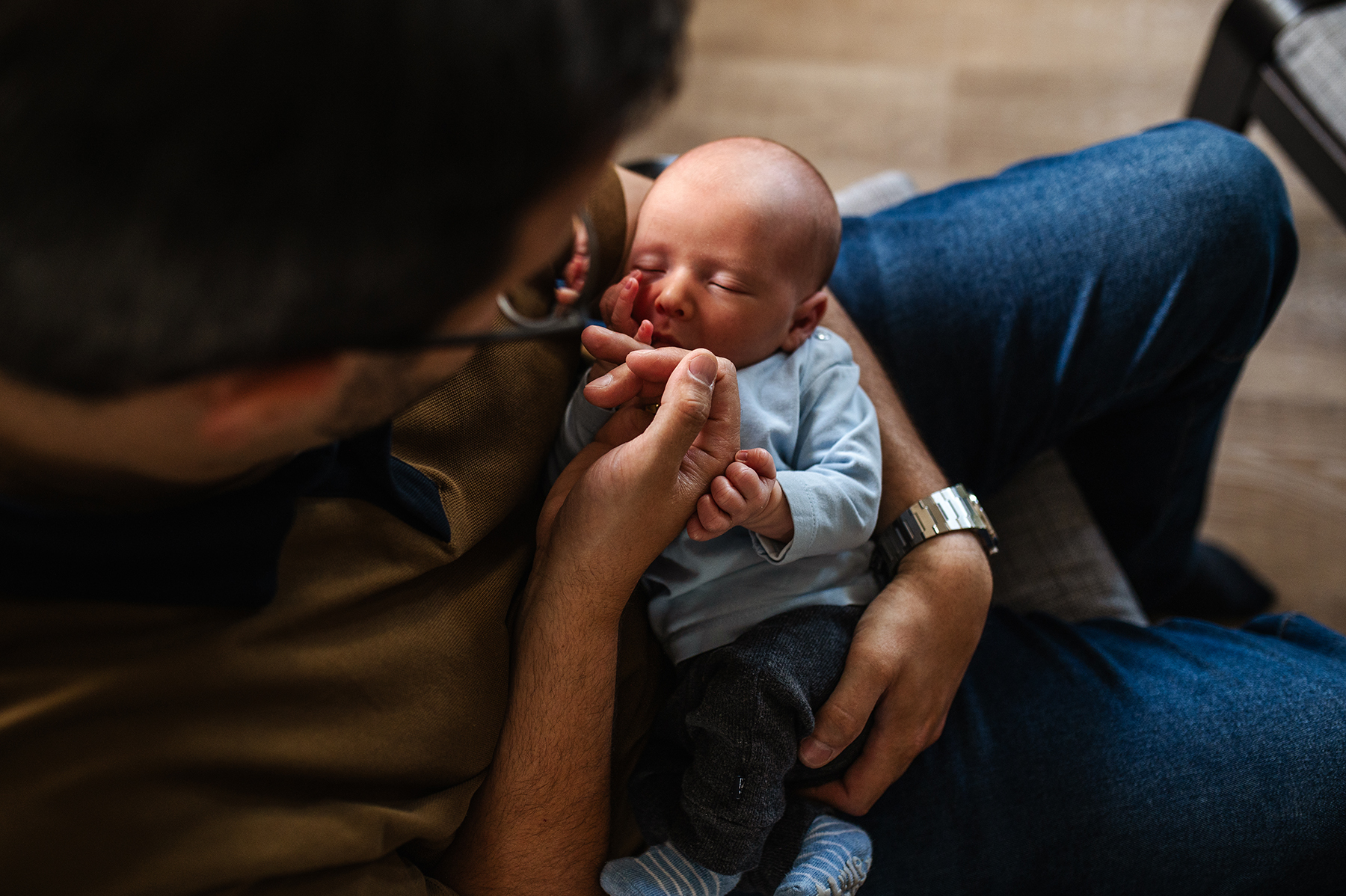 Baby nuckelt am Finger auf dem Arm vom Papa bei Neugeborenemshooting